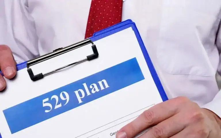 A person in a white shirt and red tie holds a clipboard with a document labeled “529 plan.” The image highlights financial planning for future education expenses, particularly savings programs designed to support college tuition and other academic costs.