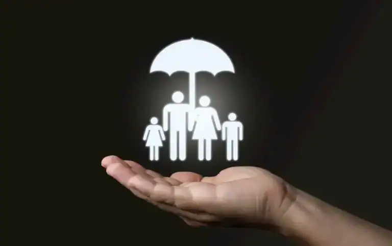 A hand held out against a dark background supports a glowing white icon of a family—two adults and two children—standing under an umbrella. The image symbolizes protection, security, and insurance coverage for loved ones.