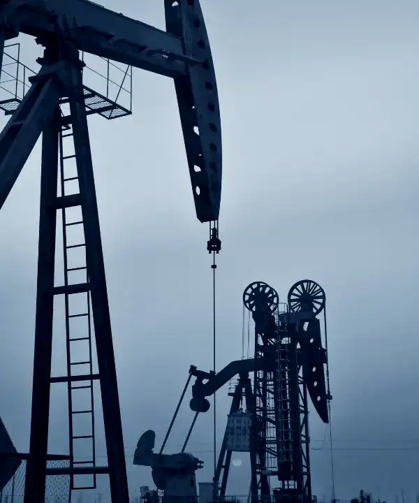 Silhouettes of oil pumpjacks operating in a field under a muted sky, representing the oil and gas industry’s foundational role in energy production and the financial challenges tied to its volatility.