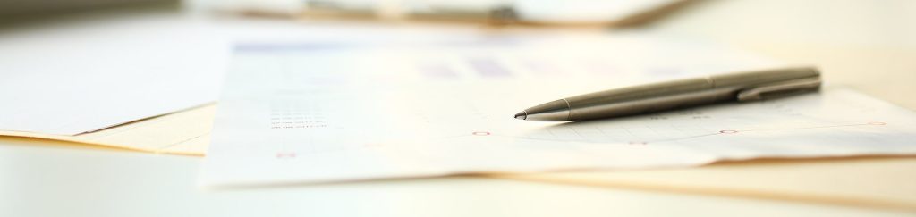 Close-up of a silver pen placed on a business report or financial document, symbolizing review or signing of a partnership agreement.