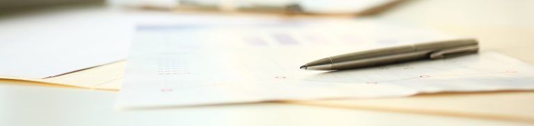 Close-up of a silver pen placed on a business report or financial document, symbolizing review or signing of a partnership agreement.