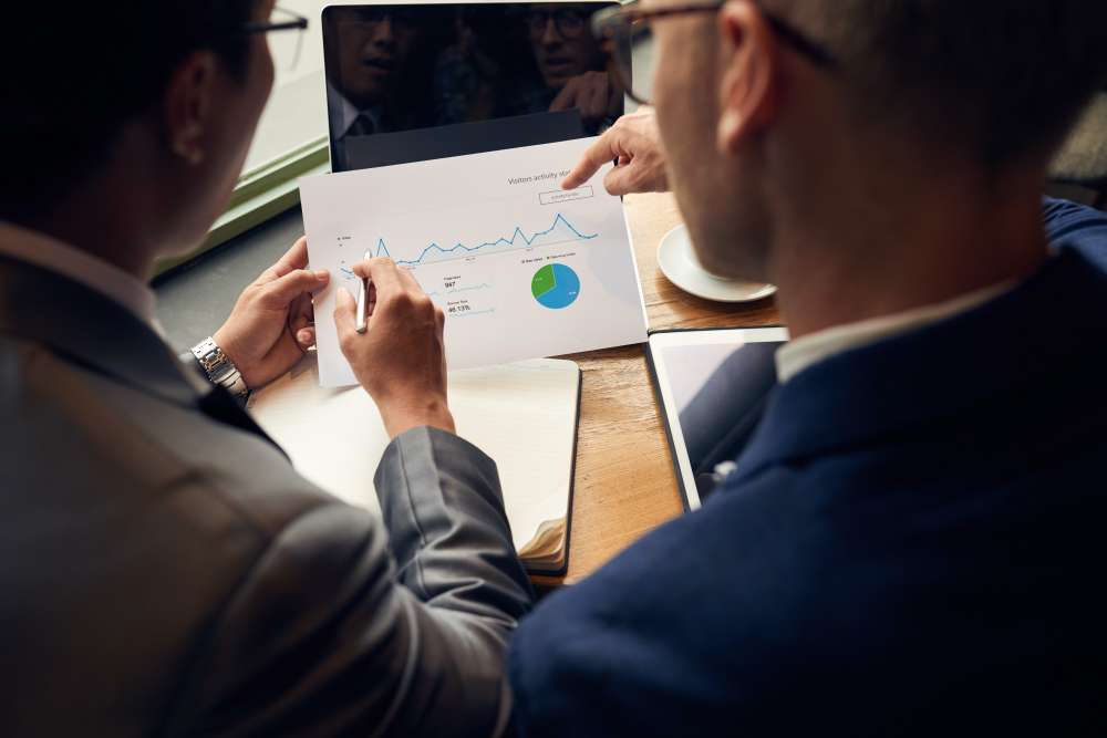 Two business professionals reviewing analytics report with charts and graphs during a meeting at a wooden desk