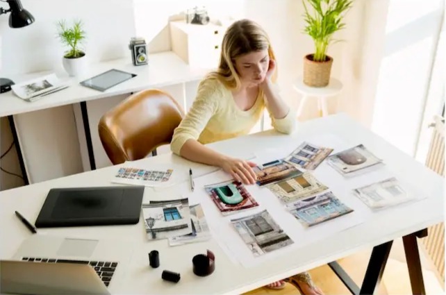 Young woman reviewing printed photographs at a desk in a bright, modern home office