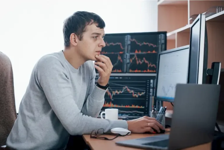 Man analyzing stock market data on multiple computer monitors in a trading setup