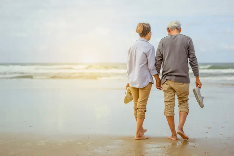 A serene image of a retired couple sitting on beach chairs, enjoying a sunset over the sea.