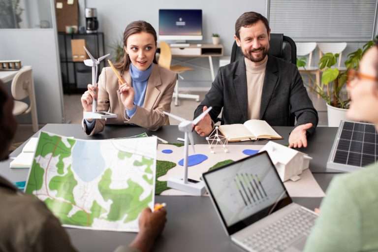 Group of professionals discussing renewable energy project using wind turbine models, solar panel samples, and environmental maps in a modern office setting